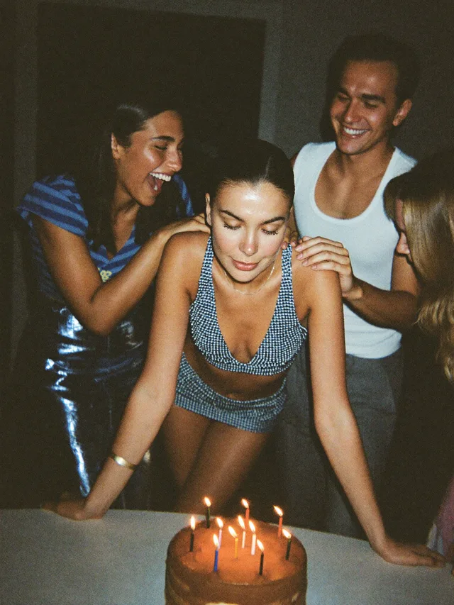 A birthday wish over lit candles, friends leaning in