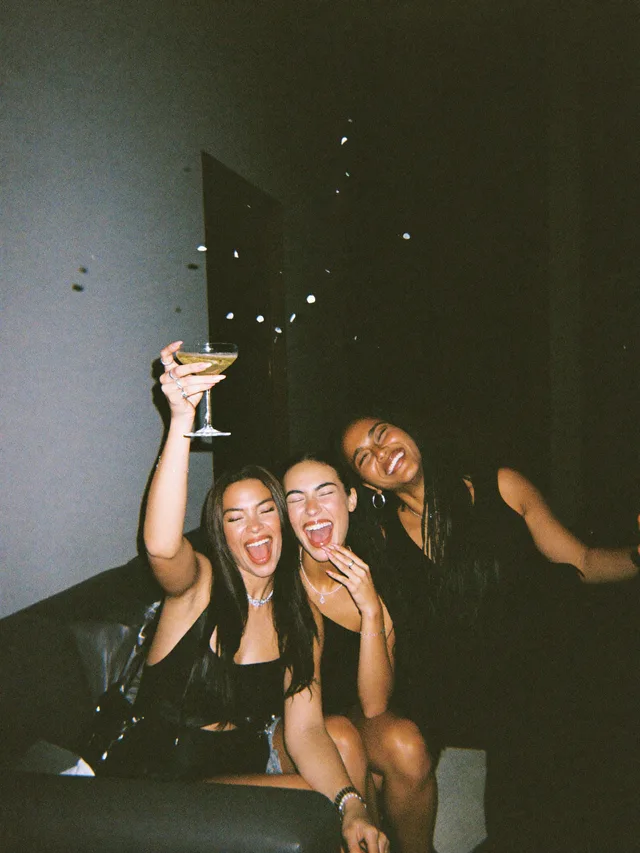 Three friends on a couch, champagne up, confetti falling