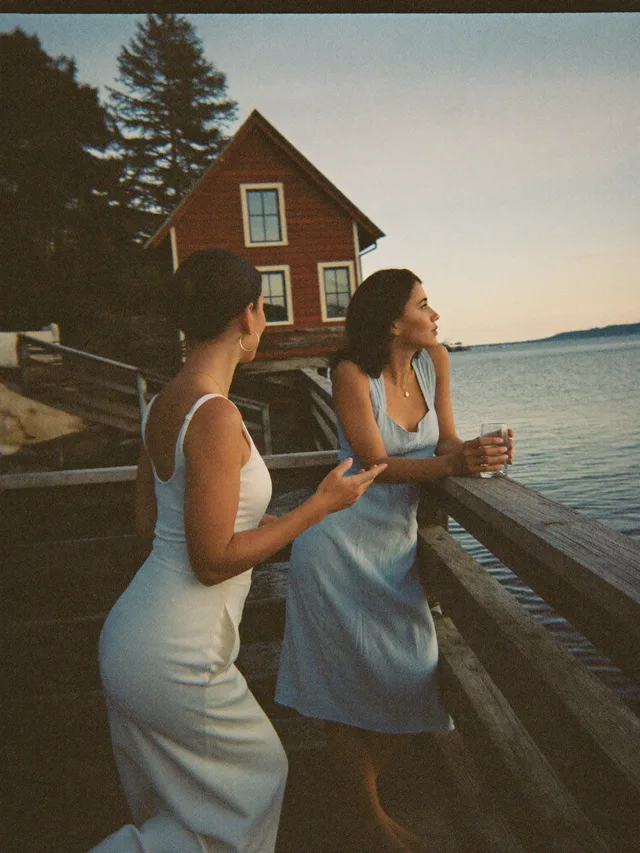 Two guests talking on a jetty railing at dusk, red cottage behind